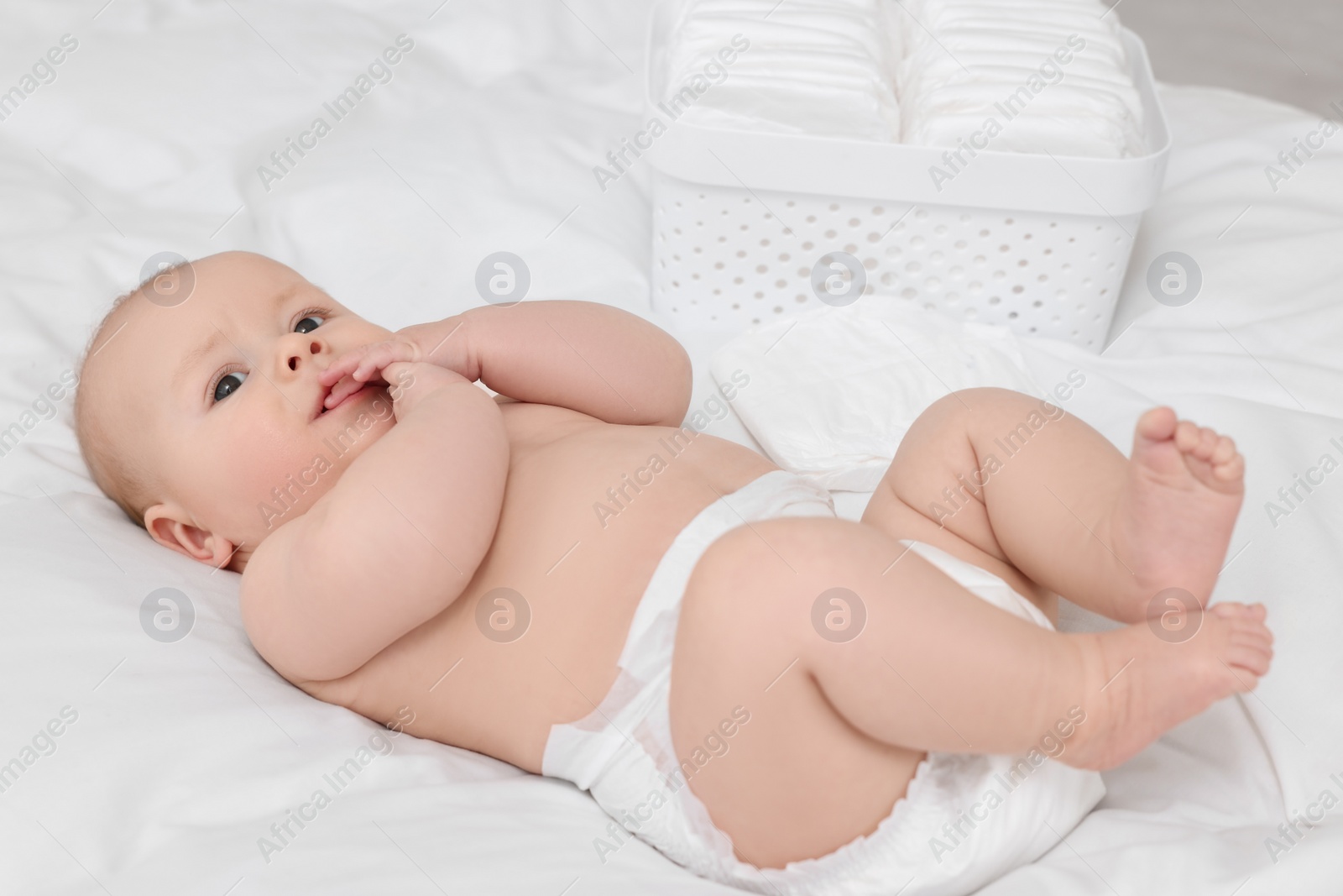 Photo of Cute baby and diapers on white bed