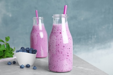 Photo of Glass bottles of blueberry smoothie and bowl with fresh berries on grey marble table