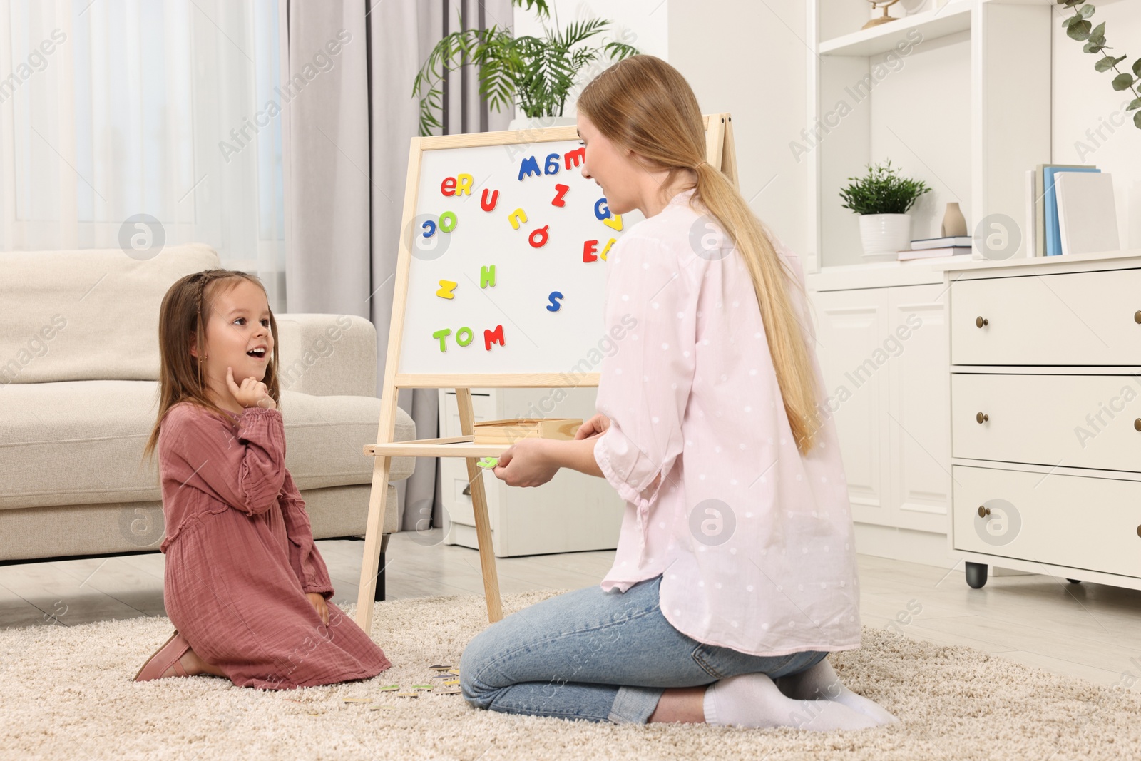 Photo of Mom teaching her daughter alphabet with magnetic letters at home