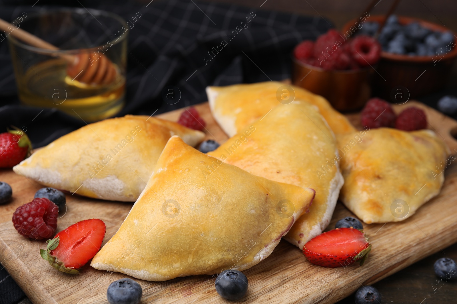 Photo of Wooden board with delicious samosas and berries on table, closeup