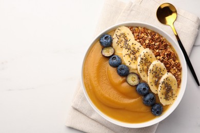 Photo of Delicious smoothie bowl with fresh blueberries, banana and granola on white table, flat lay. Space for text