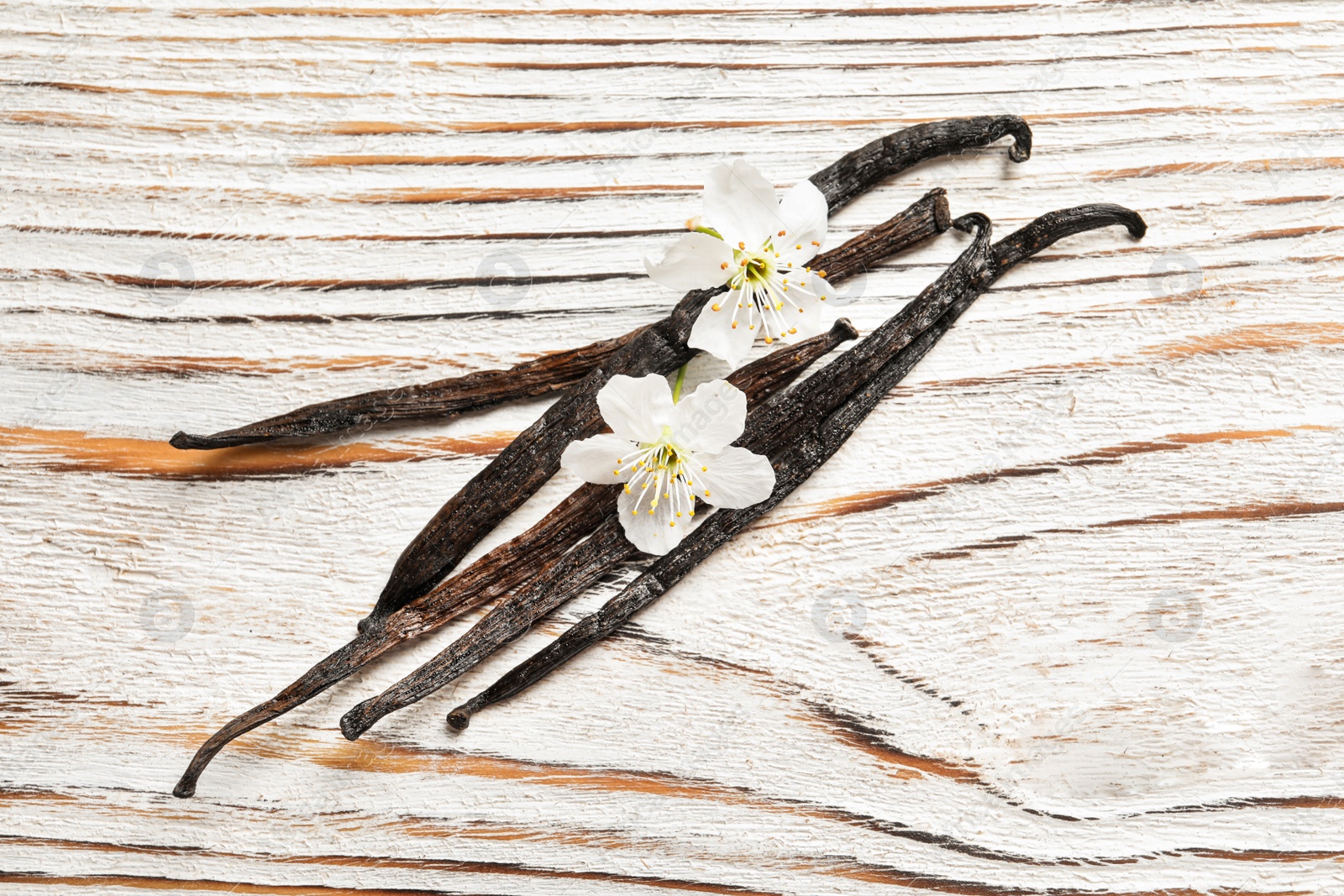 Photo of Vanilla sticks and flowers on wooden background