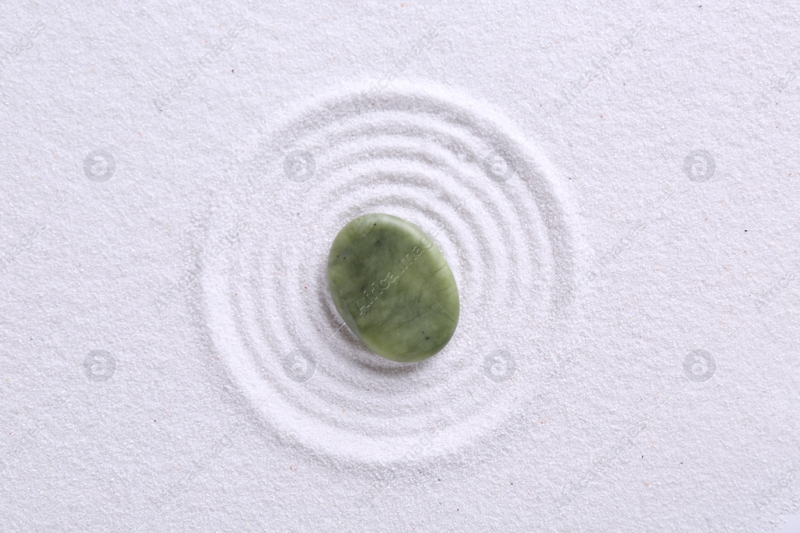 Photo of Zen garden stone on white sand with pattern, top view