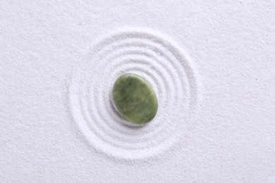 Photo of Zen garden stone on white sand with pattern, top view