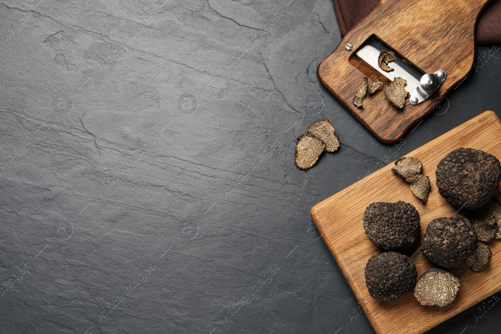 Photo of Wooden shaver with whole and sliced truffles on black table, flat lay. Space for text