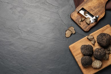 Wooden shaver with whole and sliced truffles on black table, flat lay. Space for text