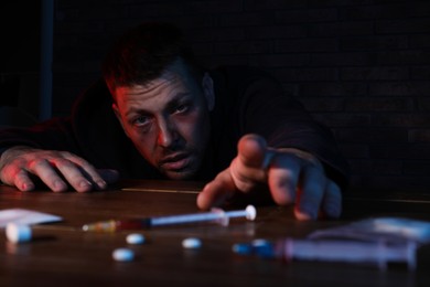 Addicted man reaching to drugs at table