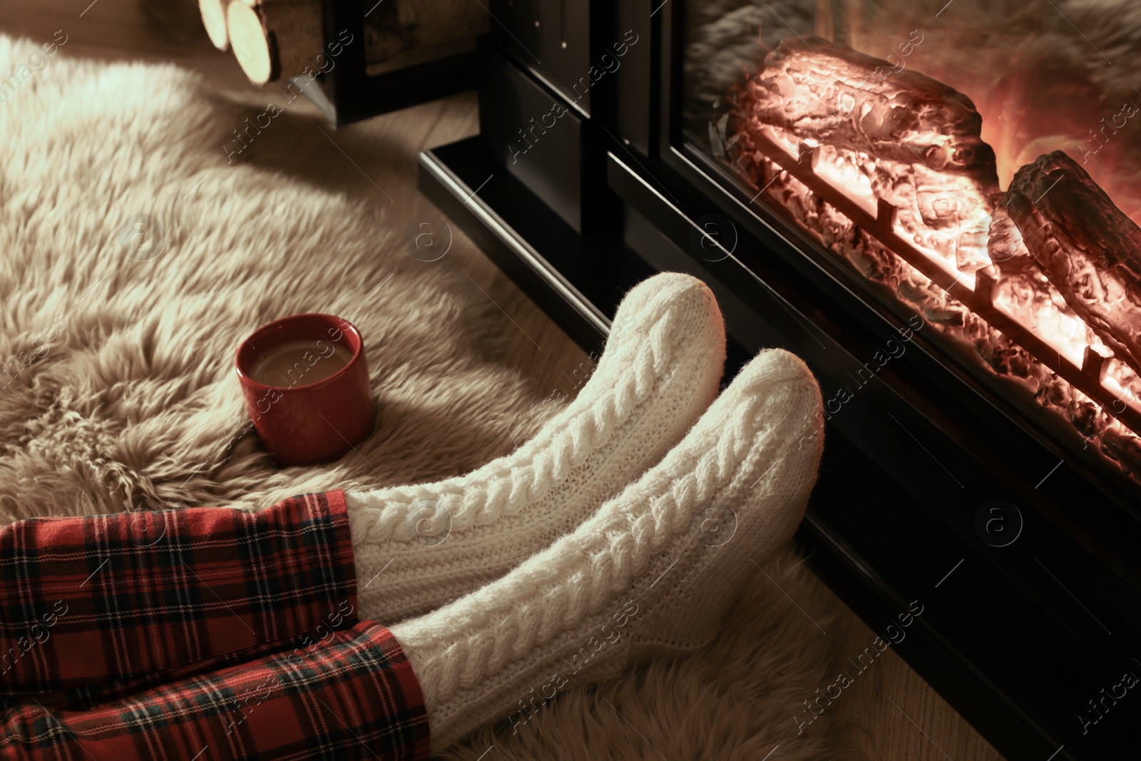 Photo of Woman in knitted socks resting near fireplace at home, closeup of legs