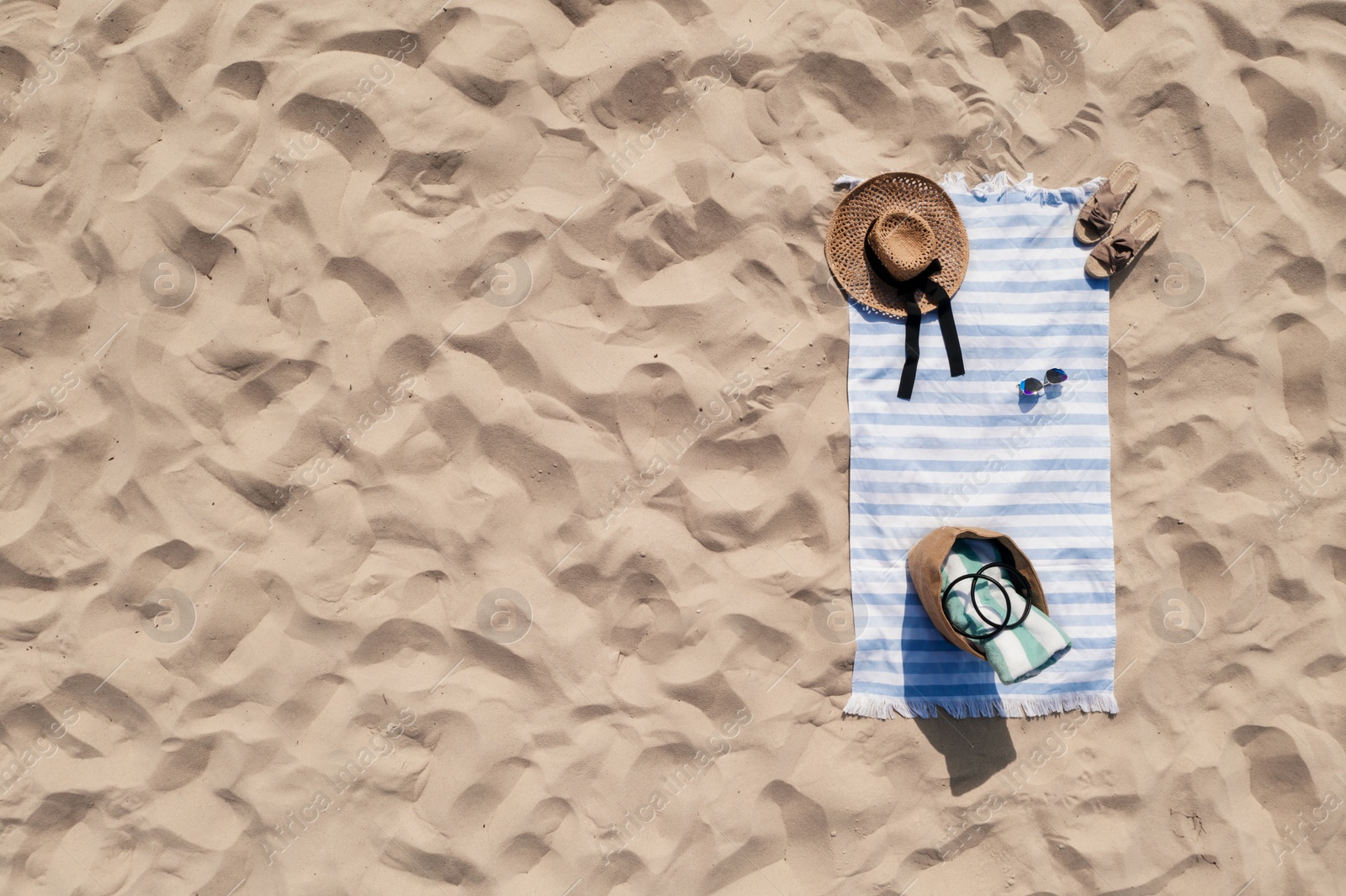 Image of Towel with beach accessories on sand, top view. Space for text