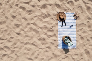 Towel with beach accessories on sand, top view. Space for text