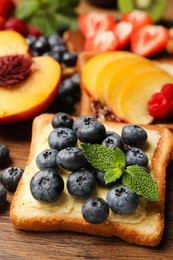 Photo of Tasty toast with butter, blueberry and mint on wooden table, closeup