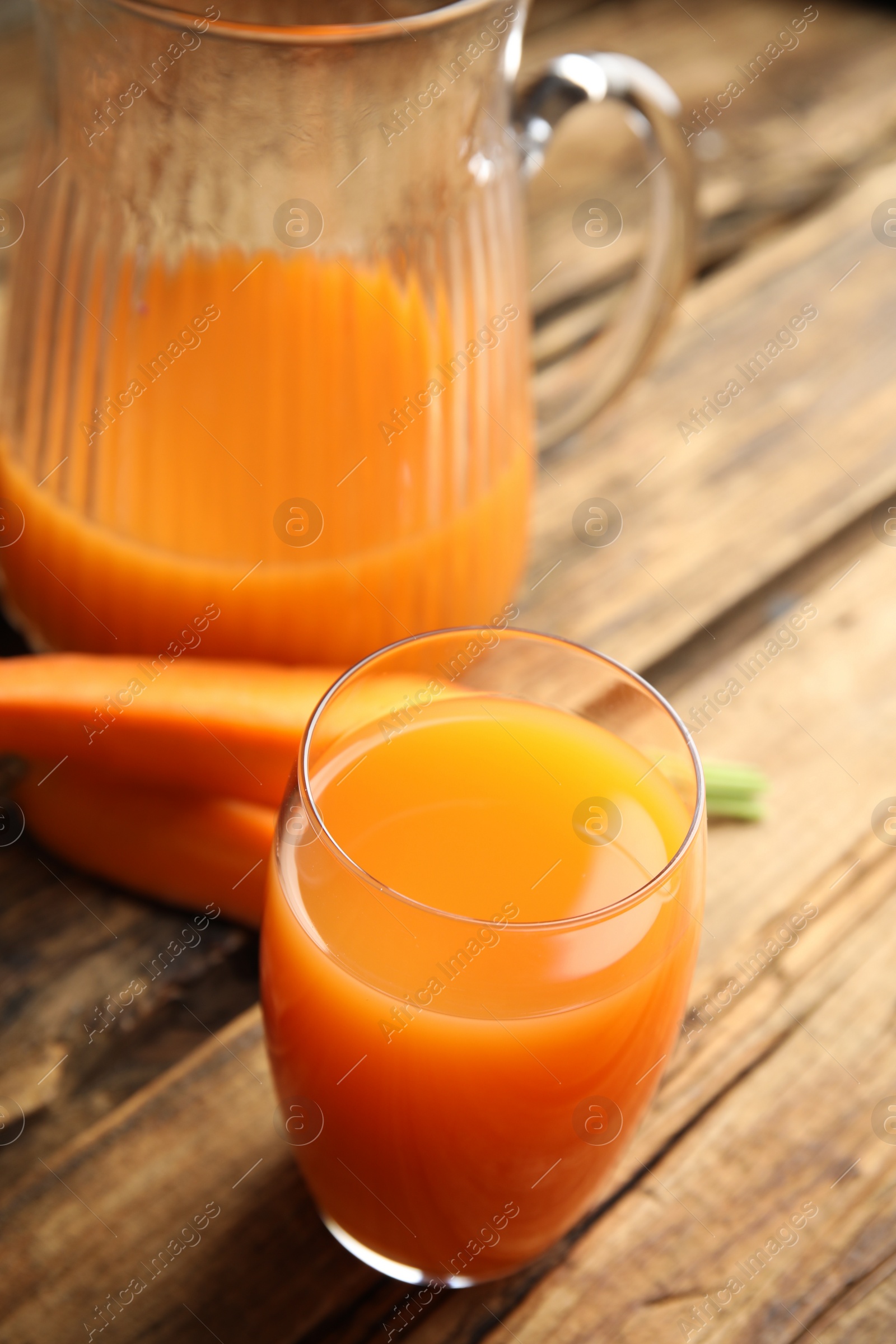 Photo of Jug and glass of freshly made carrot juice on wooden table