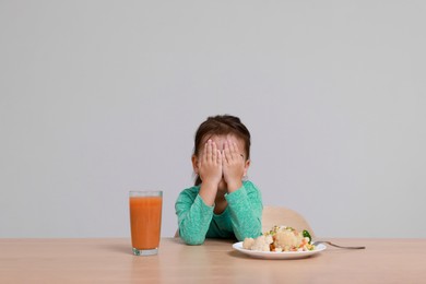 Cute little girl crying and refusing to eat vegetable salad at table on grey background