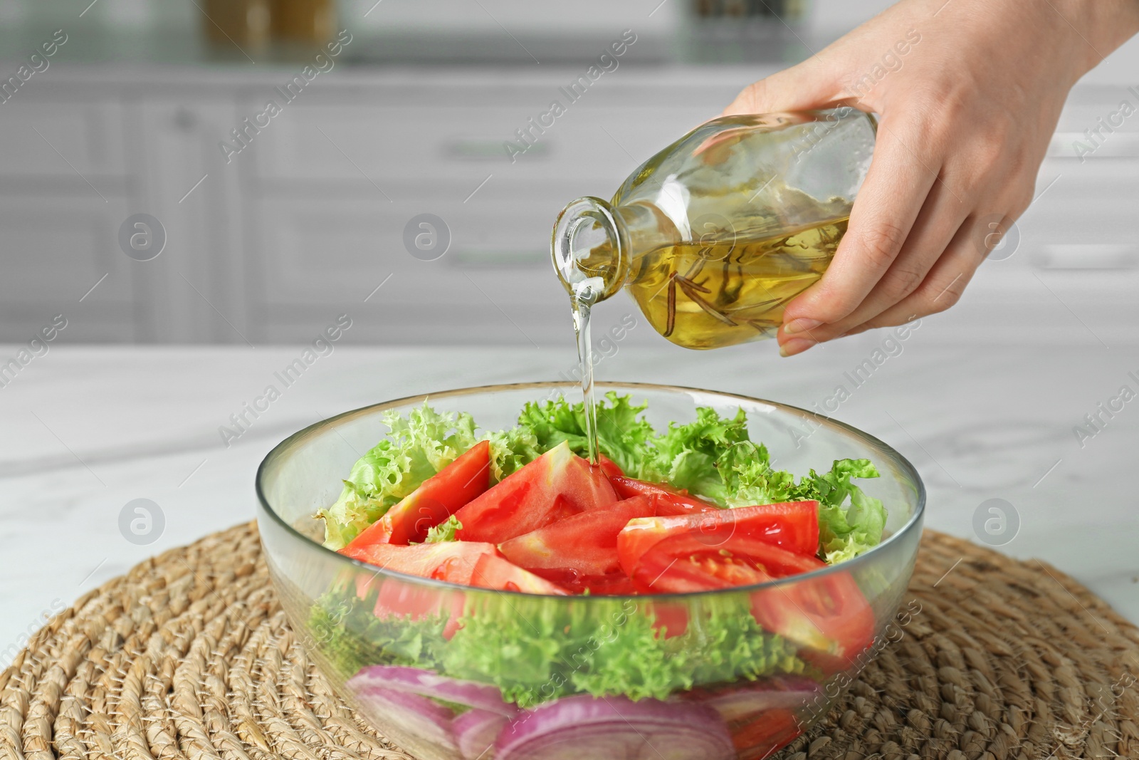 Photo of Woman pouring oil from glass bottle into bowl with salad in kitchen, closeup