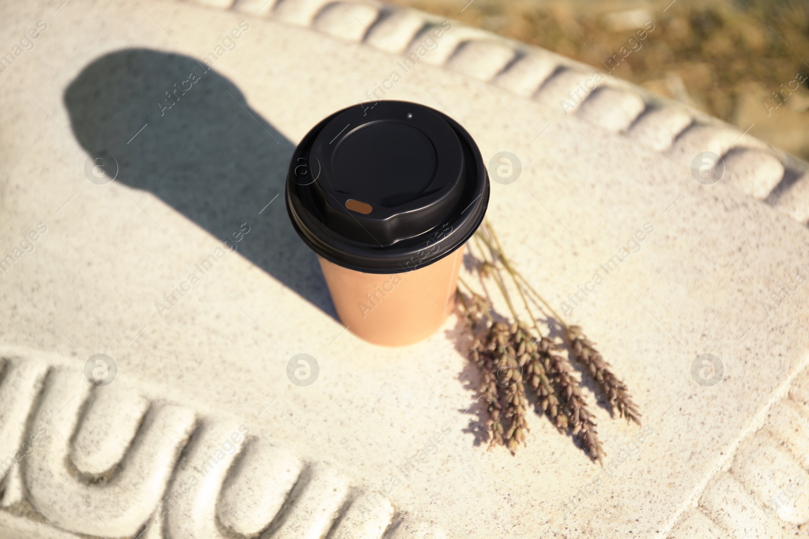 Photo of Cardboard cup with tasty coffee and dried flowers on stone bench outdoors