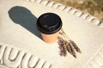 Cardboard cup with tasty coffee and dried flowers on stone bench outdoors