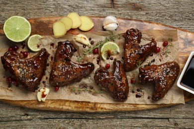 Photo of Tasty chicken wings glazed in soy sauce with garnish on wooden table, top view