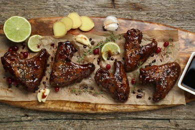 Tasty chicken wings glazed in soy sauce with garnish on wooden table, top view