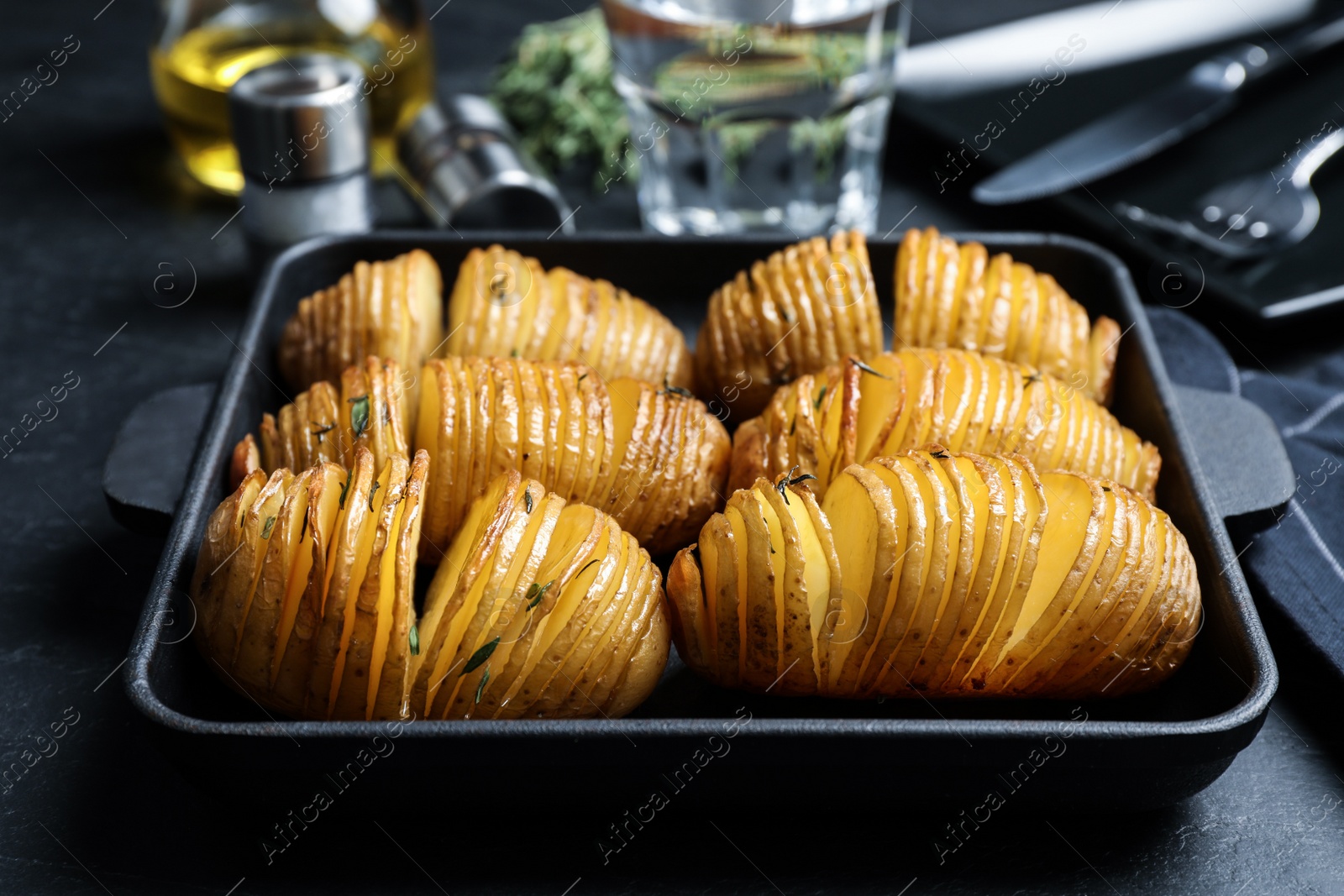 Photo of Delicious homemade Hasselback potatoes in baking pan on black table