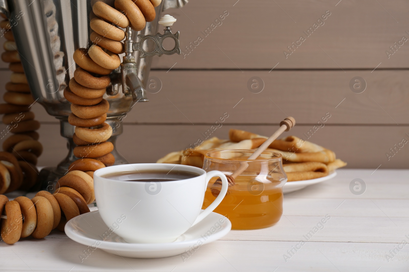 Photo of Metal samovar with cup of tea and treats on white wooden table, space for text