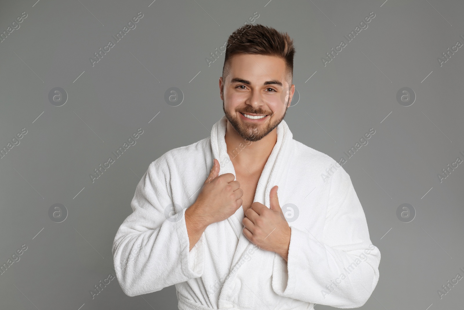 Photo of Happy young man in bathrobe on grey background