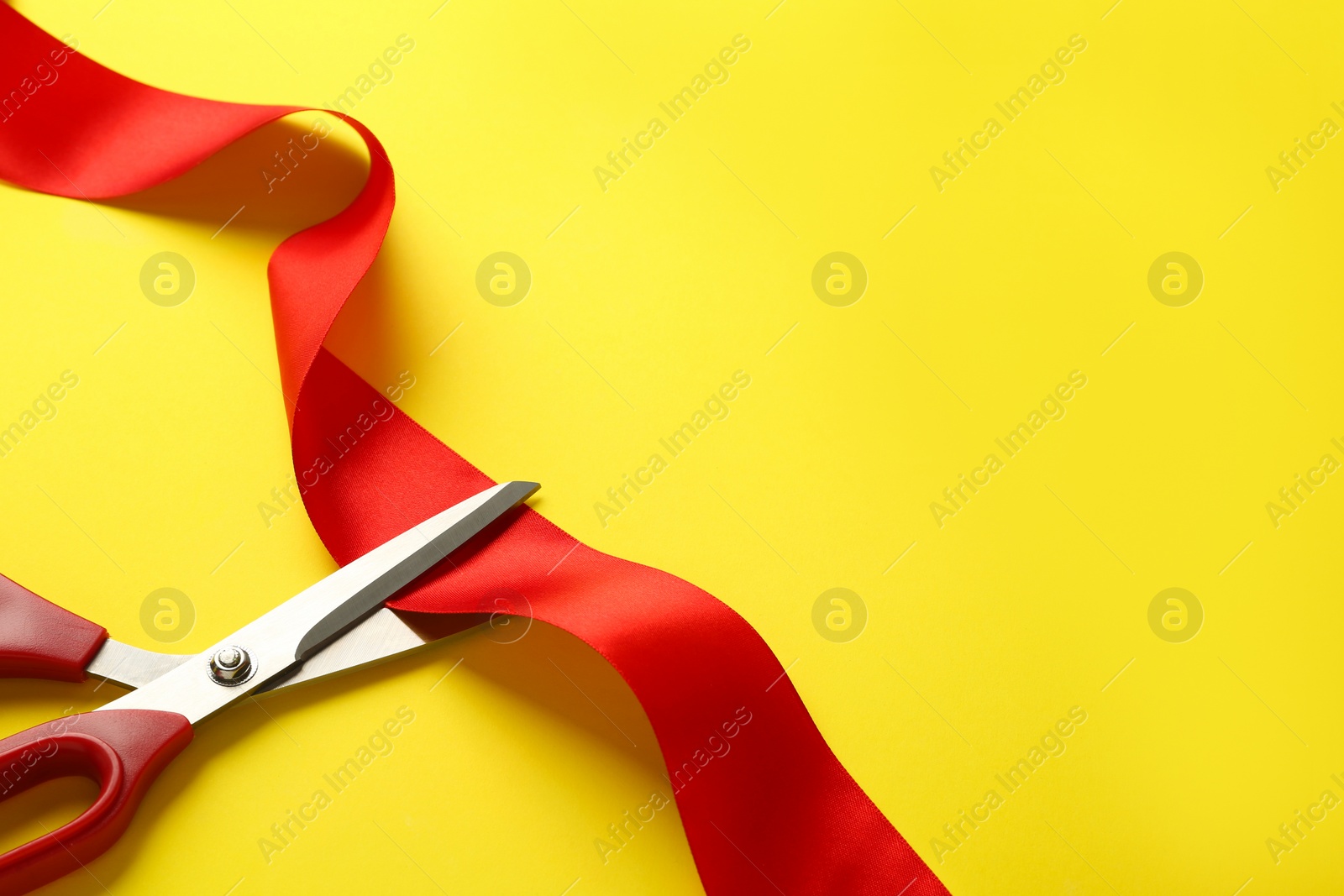 Photo of Red ribbon and scissors on yellow background, top view. Space for text