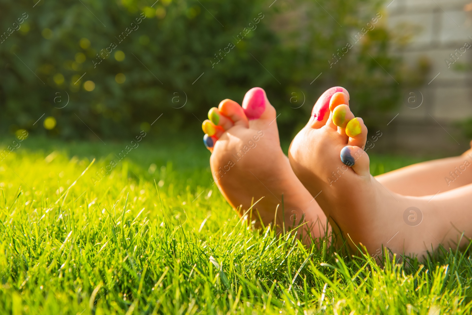 Photo of Teenage girl with painted toes on green grass outdoors, closeup. Space for text