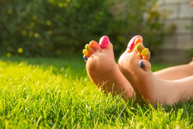 Teenage girl with painted toes on green grass outdoors, closeup. Space for text