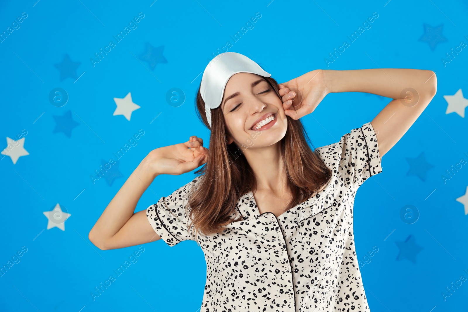 Photo of Beautiful woman wearing pajamas and sleep mask on light blue background. Bedtime