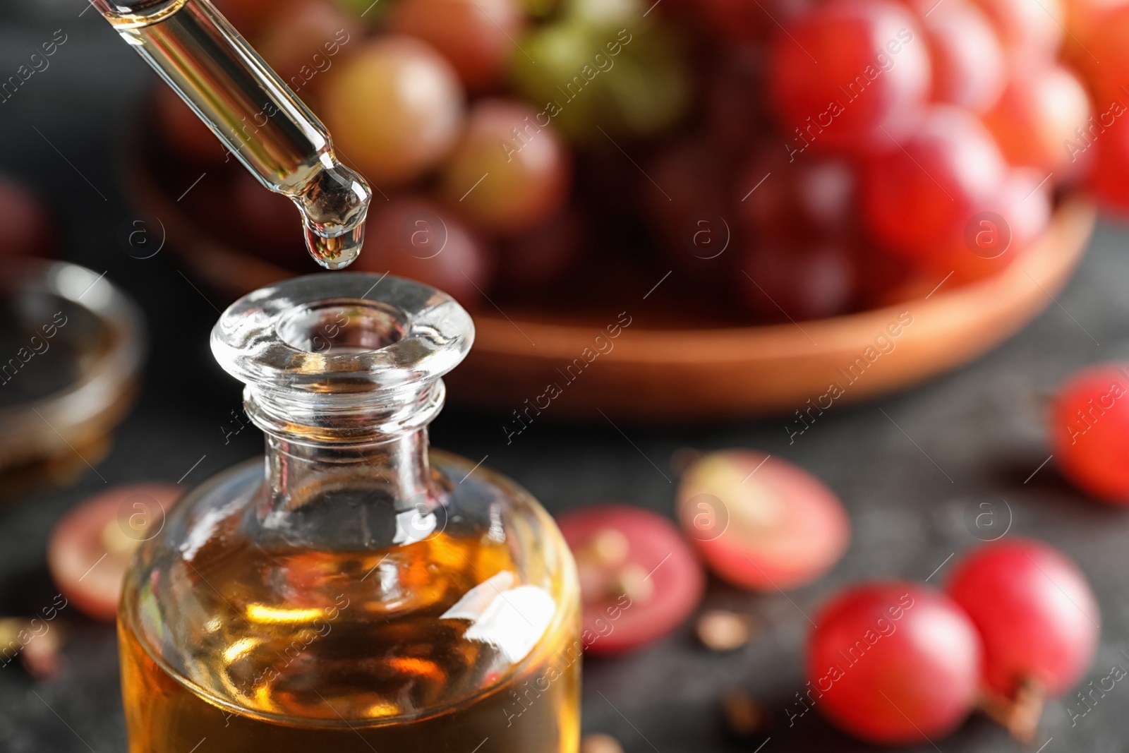 Photo of Dripping natural grape seed oil from pipette into glass bottle on table, closeup with space for text. Organic cosmetic