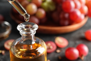 Dripping natural grape seed oil from pipette into glass bottle on table, closeup with space for text. Organic cosmetic