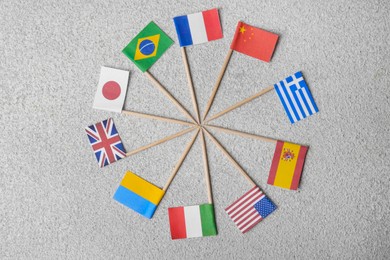 Many small paper flags of different countries on grey textured table, flat lay