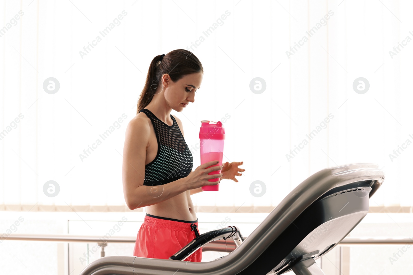 Photo of Athletic young woman with protein shake on running machine in gym