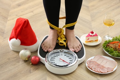 Photo of Woman using scale surrounded by food and alcohol on floor, closeup. Overweight problem after New Year party