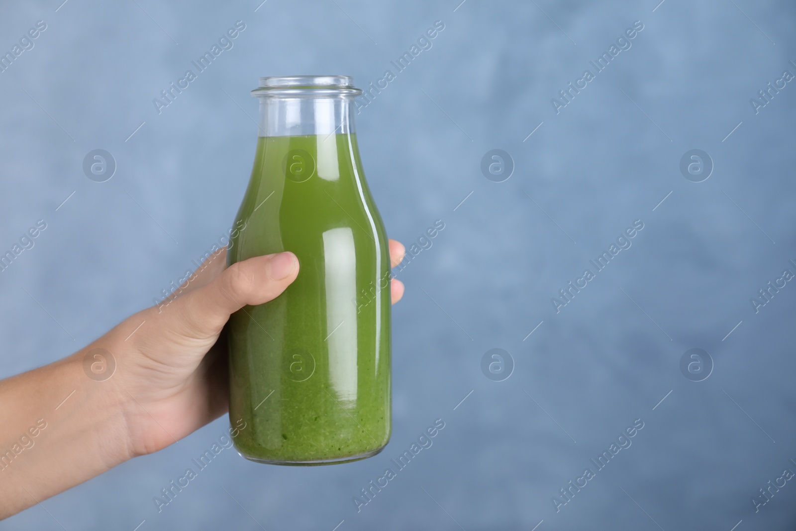 Photo of Woman holding glass bottle of fresh celery juice against blue background, closeup. Space for text