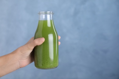 Photo of Woman holding glass bottle of fresh celery juice against blue background, closeup. Space for text