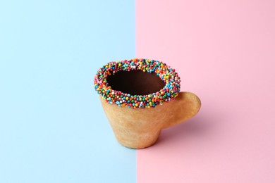 Photo of Delicious edible biscuit coffee cup decorated with sprinkles on color background