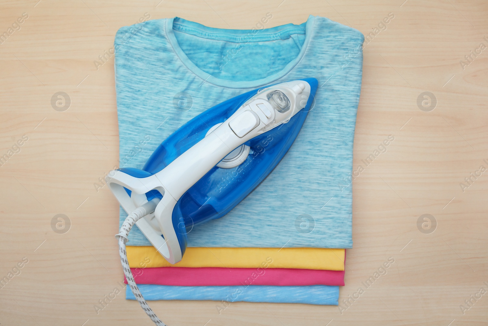 Photo of Folded clean clothes and iron on wooden background, top view