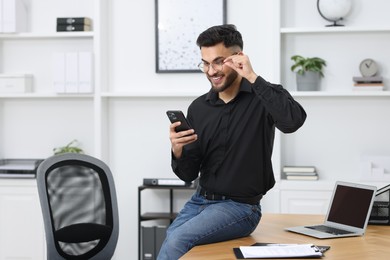 Photo of Happy young man using smartphone in office