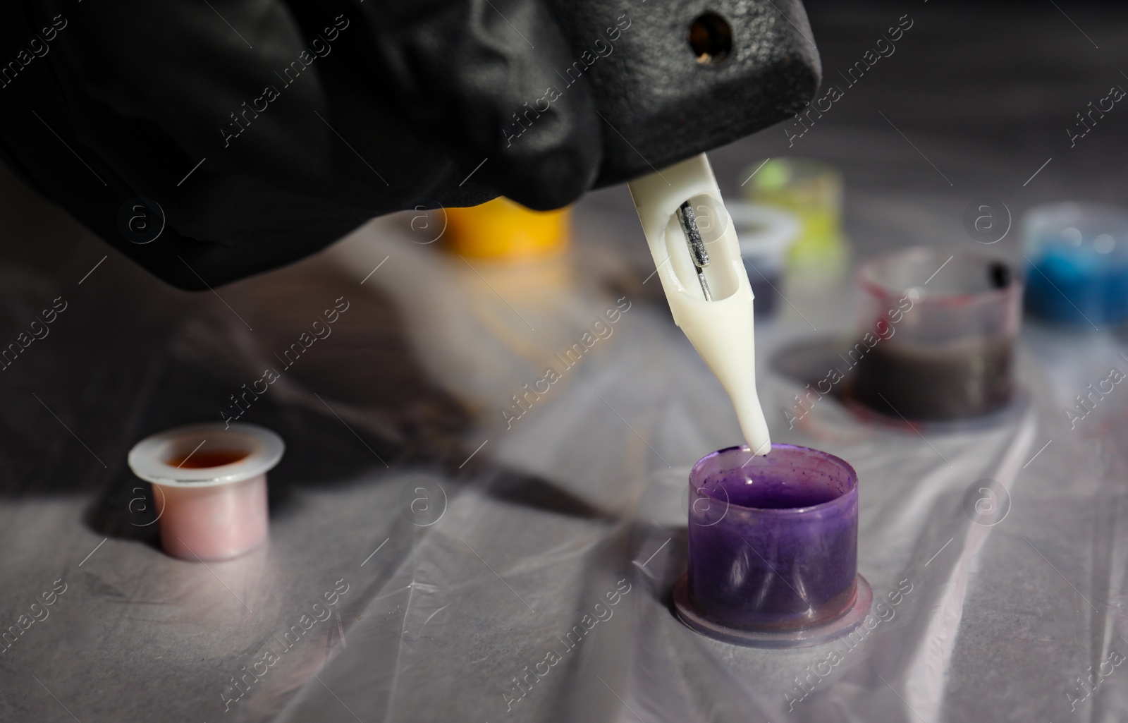 Photo of Tattoo artist dipping machine needle into ink at table, closeup