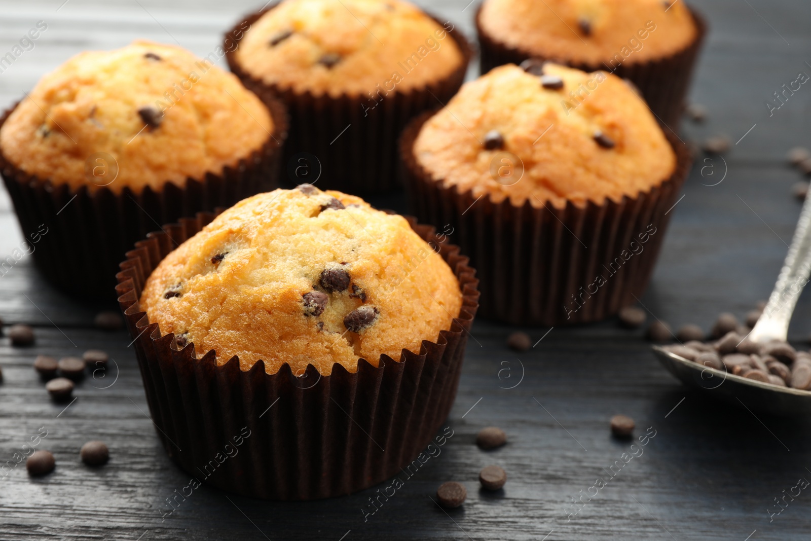 Photo of Delicious freshly baked muffins with chocolate chips on dark gray table, closeup