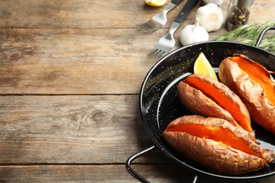 Dish with baked sweet potatoes on wooden table. Space for text