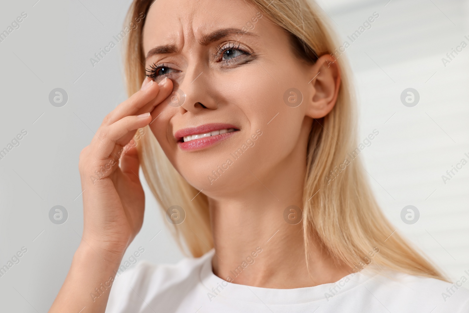 Photo of Sad woman with smeared mascara crying indoors, closeup