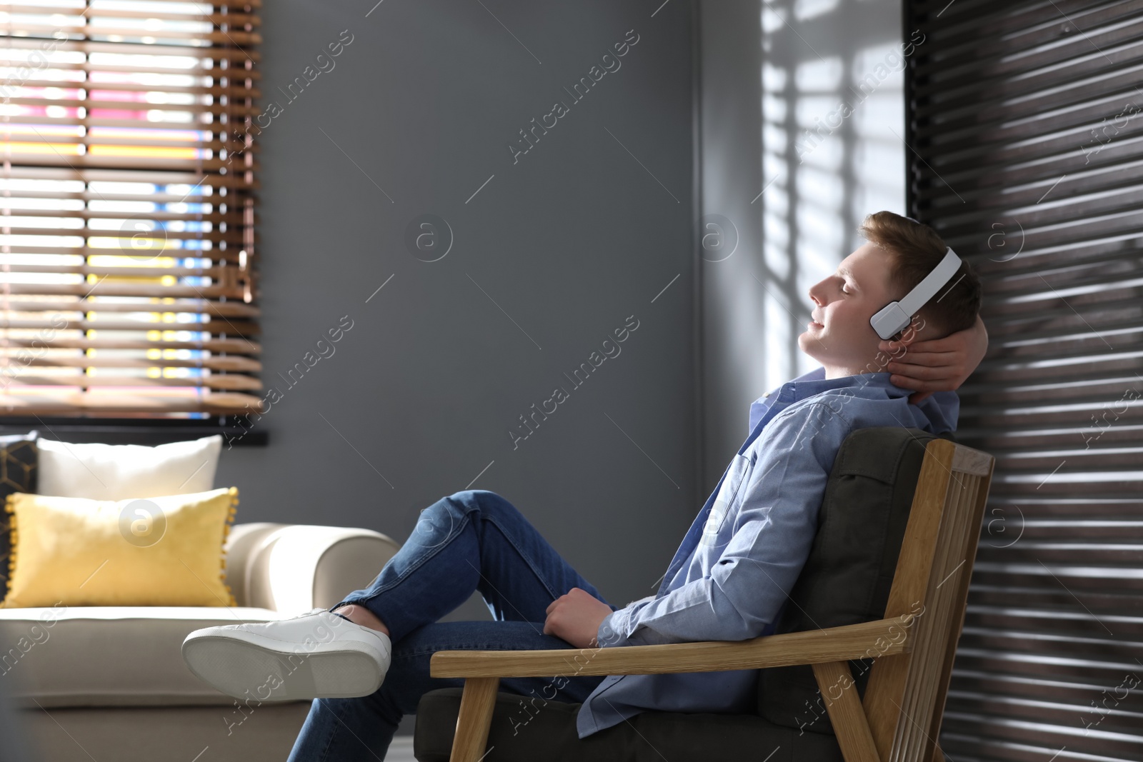 Photo of Teenage boy with headphones listening to music in armchair at home