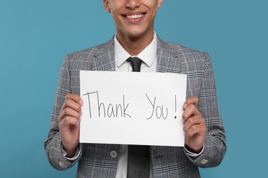 Photo of Man holding card with phrase Thank You on light blue background, closeup