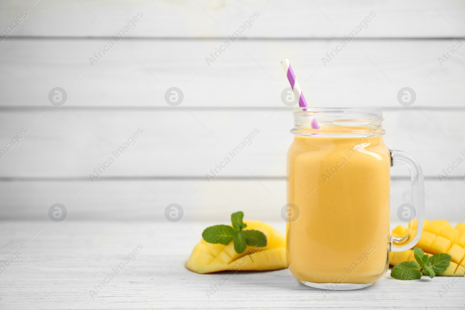 Photo of Fresh delicious mango drink on white wooden table. Space for text