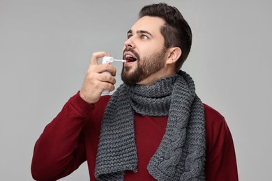 Photo of Young man with scarf using throat spray on grey background