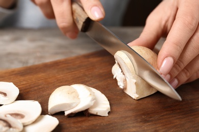 Photo of Young woman cutting fresh champignon mushrooms on wooden board, closeup view