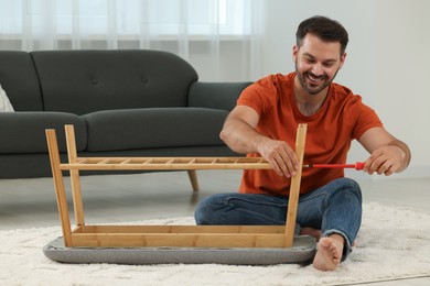 Photo of Man assembling shoe storage bench with screwdriver on floor at home