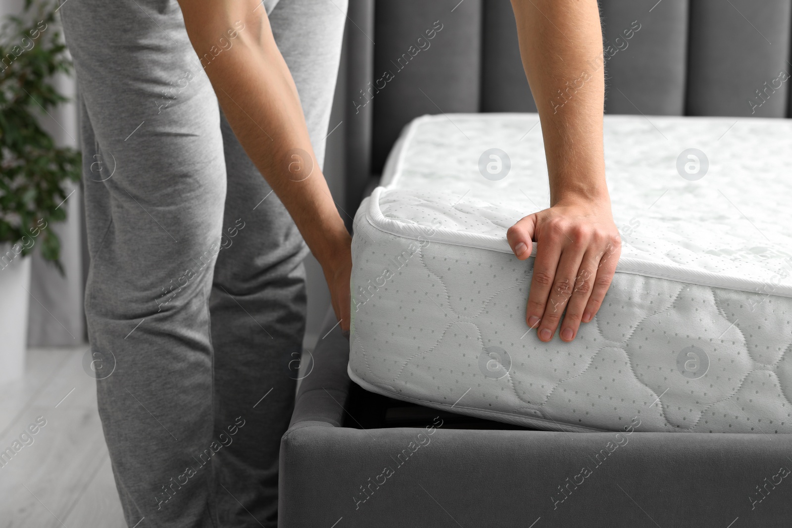 Photo of Man putting soft mattress on bed, closeup